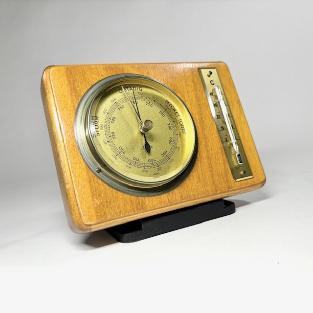 Lyxig Barometer och termometer på träplatta med svarvad kant tidigt 1950-tal av Genia Optik märkt no 2127. Optik med matt mässing, ev förgylld metall i matt textur, glas och metallram. Svensk tavla.
